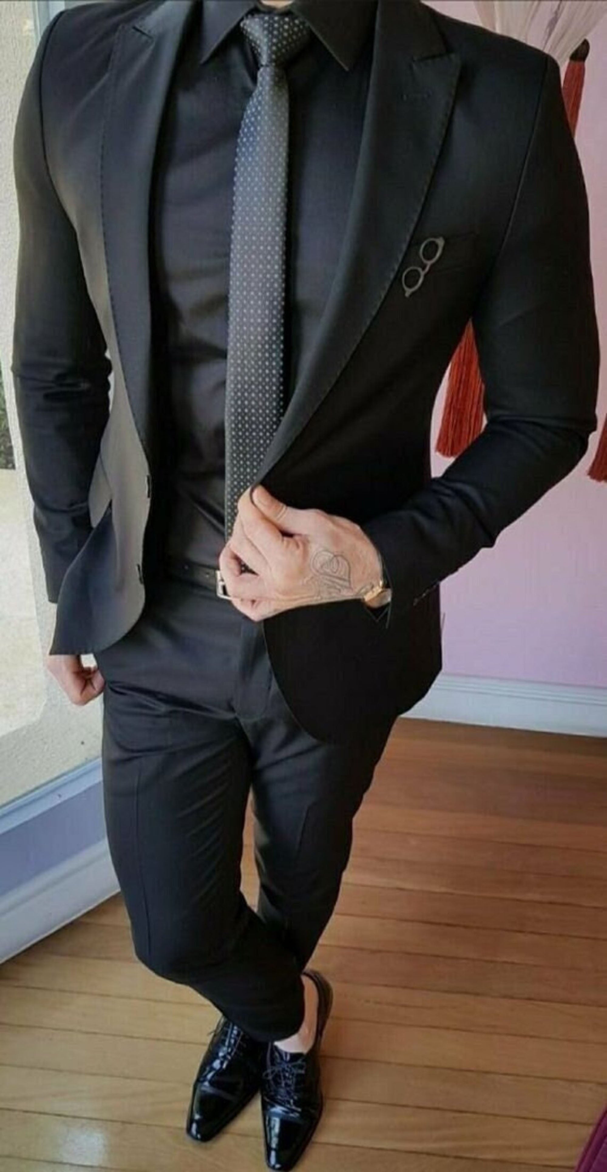 Men's black single-breasted suit with peak lapel and two-button closure.